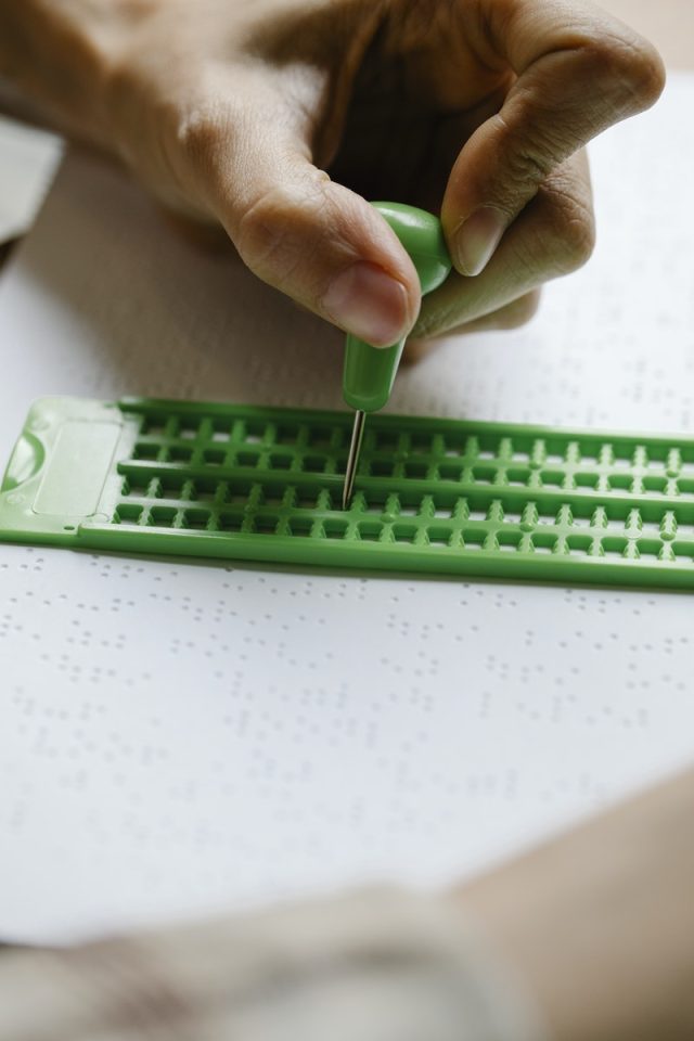 Closeup of crop anonymous blind person writing text with Braille slate and stylus