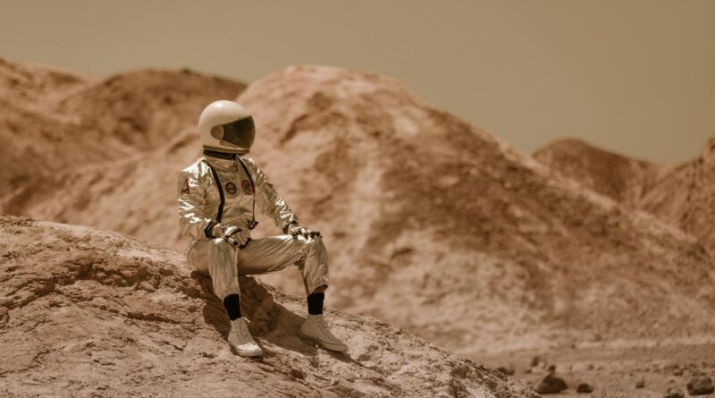 A Man in Space Suit Sitting on a Rock