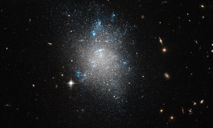 Popis: Na snímku se nachází NGC 5477, jedna z trpasličích galaxií ve skupině Messier 101, která je předmětem tohoto snímku z Hubbleova vesmírného dalekohledu NASA/ESA. Bez zjevné struktury, ale s viditelnými známkami probíhajícího zrodu hvězd, vypadá NGC 5477 velmi podobně jako typická trpasličí nepravidelná galaxie. Tento snímek je kombinací expozic pořízených přes zelené a infračervené filtry pomocí Hubbleova dalekohledu Advanced Camera for Surveys. Zorné pole je přibližně 3,3 x 3,3 úhlových minut.