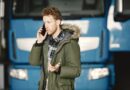 Man in a green parka talking on the phone in front of a blue truck.