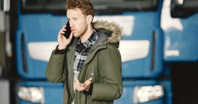 Man in a green parka talking on the phone in front of a blue truck.