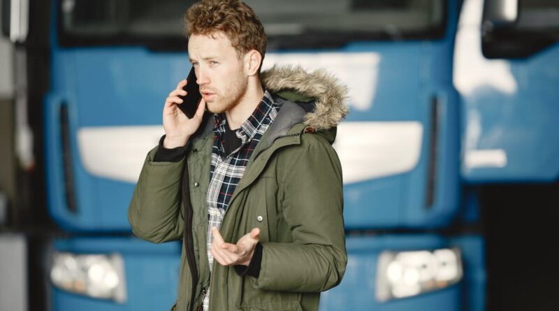 Man in a green parka talking on the phone in front of a blue truck.